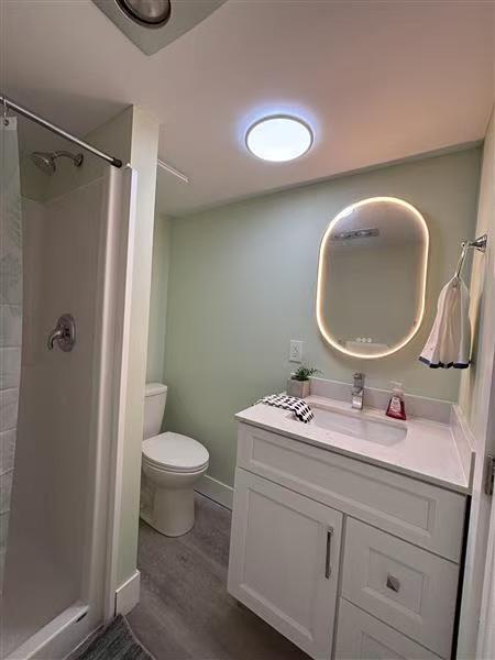 Clean guest bathroom with shower stall, illuminated mirror, and crisp linens