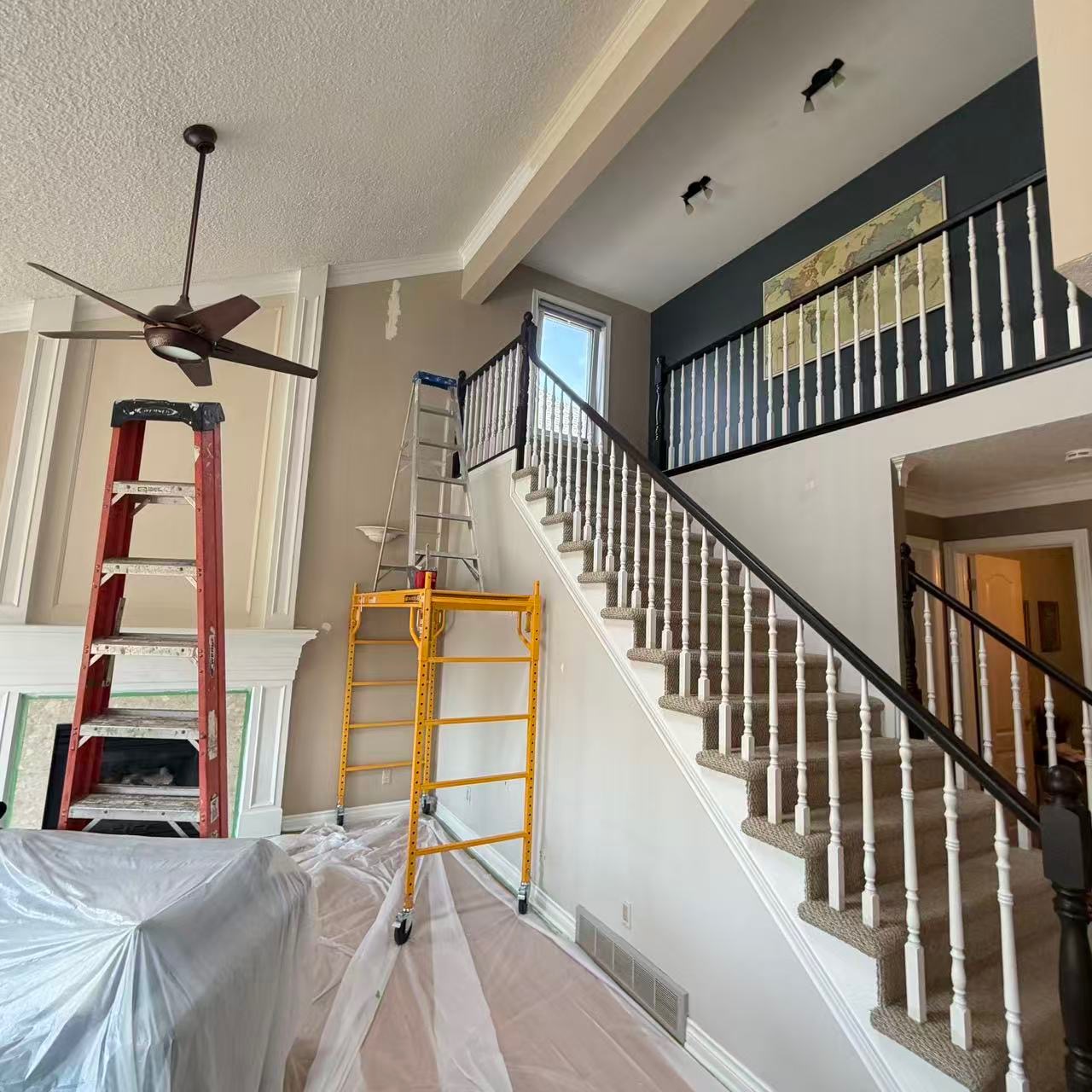 Interior of a home mid-renovation with ladders, drop cloths, and a grand staircase